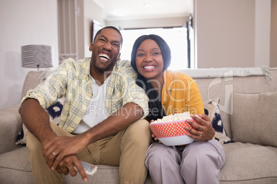 Cheerful young couple watching television while sitting on sofa at home