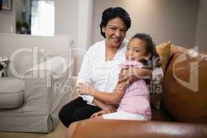 Portrait of grandmother and granddaughter embracing on sofa at home