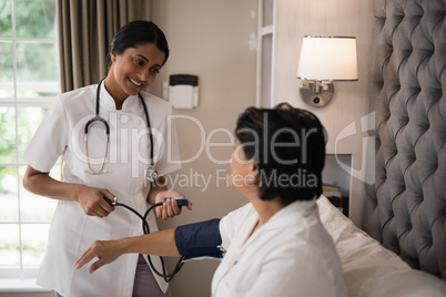 Smiling nurse checking blood pressure of patient resting on bed