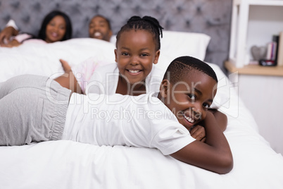 Portrait of smiling siblings lying with parents in background