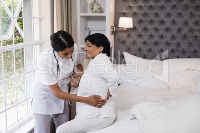 Nurse assisting female patient suffering with back pain on bed