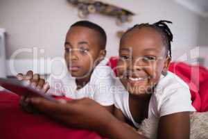 Cheerful girl with brother using mobile phone on bed at home