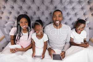 Portrait of smiling family holding digital tablets on bed