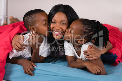 Siblings kissing their mother while lying on bed