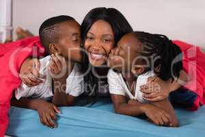 Siblings kissing their mother while lying on bed
