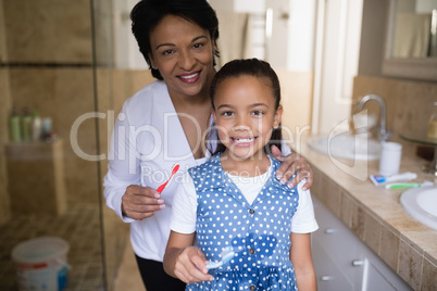 Smiling girl with grandmother holding toothbrushes in bathroom