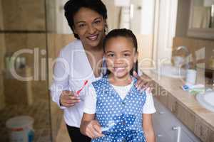 Smiling girl with grandmother holding toothbrushes in bathroom