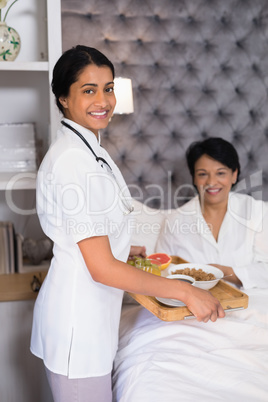 Portrait of smiling nurse giving breakfast to patient resting on bed
