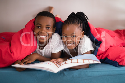 Portrait of smiling siblings holding book together on bed