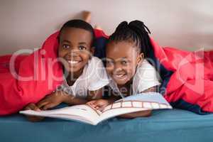 Portrait of smiling siblings holding book together on bed