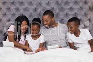 Happy family using digital tablets together on bed