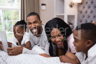 Portrait of man holding laptop while lying with family on bed