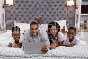 Portrait of smiling family using laptop while lying together on bed