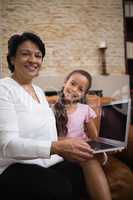 Portrait of smiling woman with granddaughter holding laptop at home