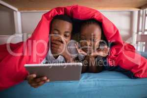 Surprised siblings holding digital tablet while lying on bed