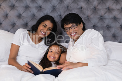 Portrait of smiling multi-generation family with book resting on bed