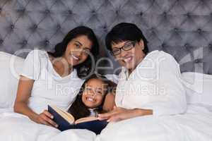 Portrait of smiling multi-generation family with book resting on bed