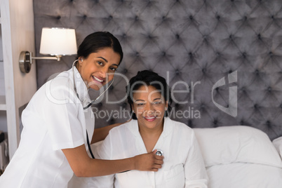 Smiling nurse examining mature woman resting on bed at home