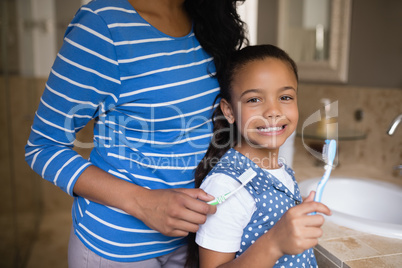 Smiling girl with mother brushing teeth in bathroom