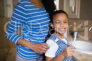 Smiling girl with mother brushing teeth in bathroom
