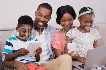 Family using technologies while sitting on sofa at home