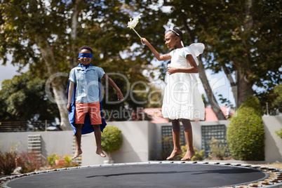 Siblings in costumes jumping on trampoline