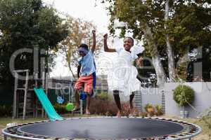 Playful siblings in costumes enjoying on trampoline