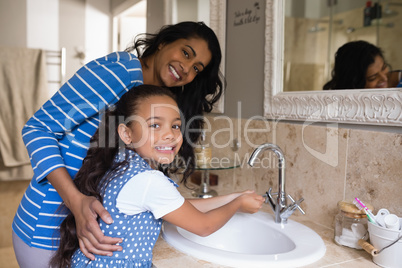 Smiling girl with mother washing hands at bathroom sink