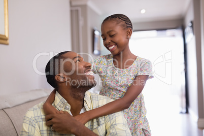 Smiling father and daughter sitting on sofa in living room