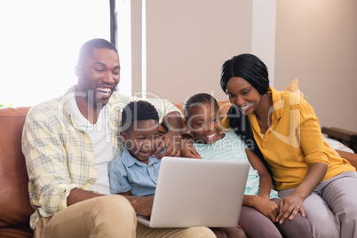 Happy parents and children using laptop while sitting on sofa