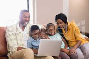 Happy parents and children using laptop while sitting on sofa