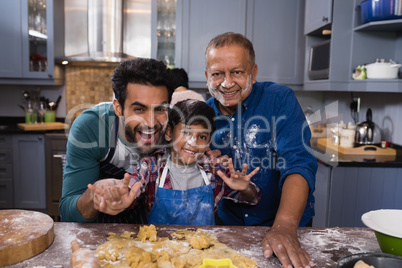 Portrait of multi-generation family standing by dough in kitchen
