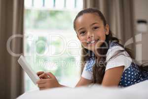 Girl using digital tablet while lying on bed at home