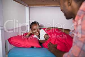 Father talking to daughter lying on bed at home