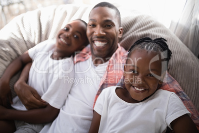 High angle portrait of happy father with daughter and son resting on couch