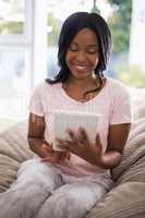 Smiling young woman using digital tablet while sitting on couch
