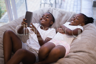 Happy siblings using mobile phone while lying on couch