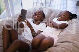 Happy siblings using mobile phone while lying on couch