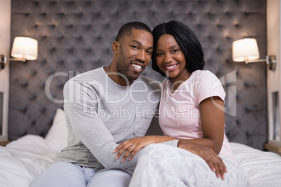 Happy young couple sitting on bed at home