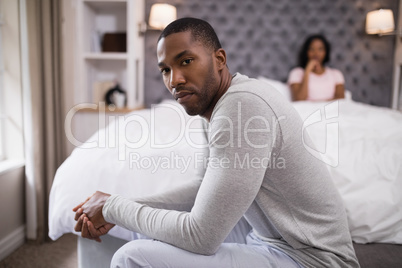 Young man siting while woman resting on bed at home