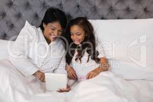 High angle view of smiling grandmother and granddaughter using digital tablet on bed