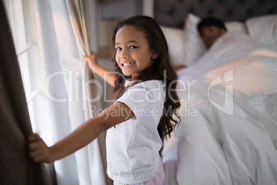 Portrait of of happy girl holding curtains in bedroom