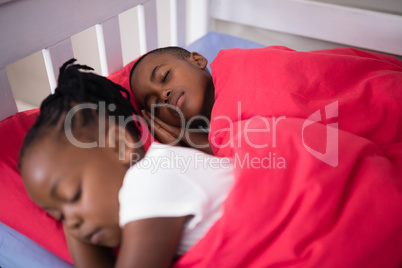 Brother and sister sleeping on bed at home
