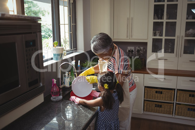 Grandmother and granddaughter washing utensil in kitchen sink