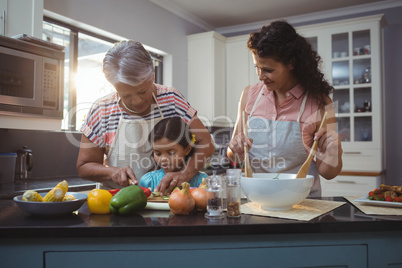 Grandmother teaching granddaughter to chop vegetables in kitchen