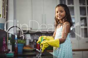 Cute little girl washing utensil in kitchen sink