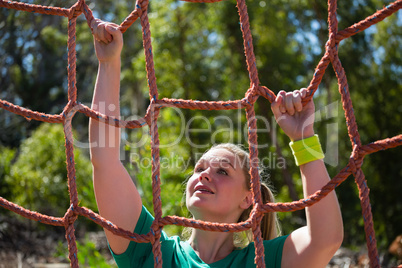 Determined woman climbing a net during obstacle course training