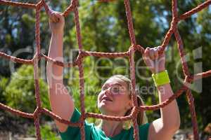 Determined woman climbing a net during obstacle course training