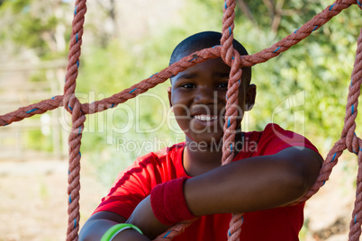 Portrait of happy boy leaning on net during obstacle course