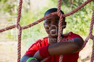 Portrait of happy boy leaning on net during obstacle course